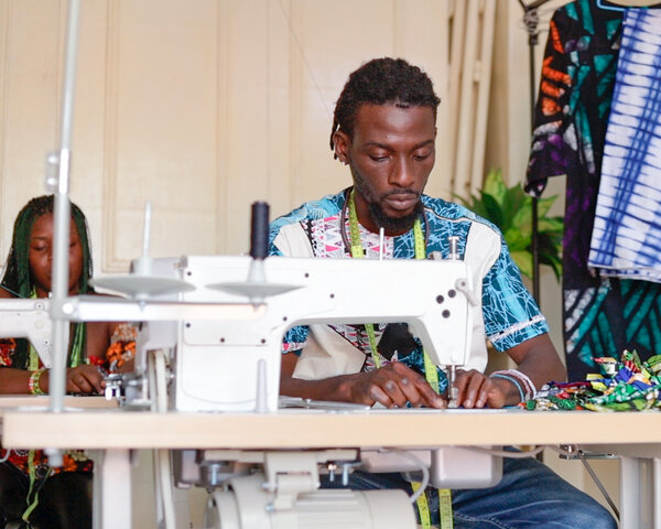 Ein Designer aus Togo sitzt vor einer Nähmaschine.