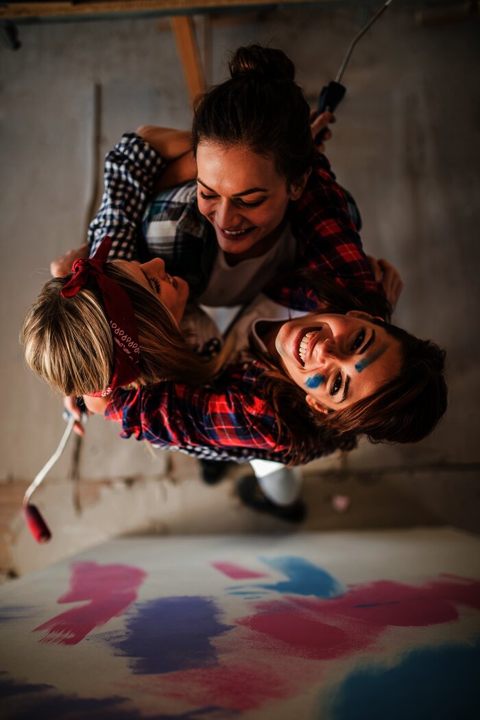 Drei Frauen halten sich fest im Arm halten und haben Streichutensilien in der Hand.