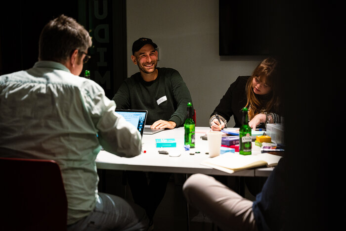 Man sieht vier Personen an einem Tisch, die sich unterhalten und miteinander lachen. Auf dem Tisch liegen verschiedenste Kreativmethoden  
