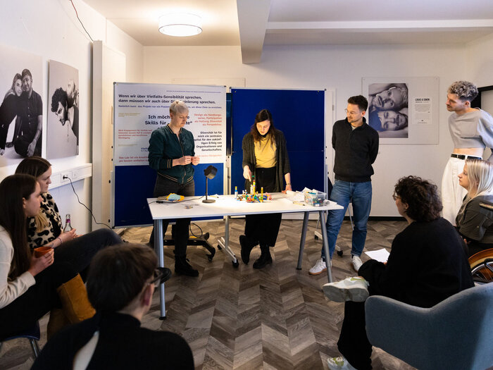 Drei Menschen präsentieren etwas mit Lego Gebasteltes vor einer Gruppe