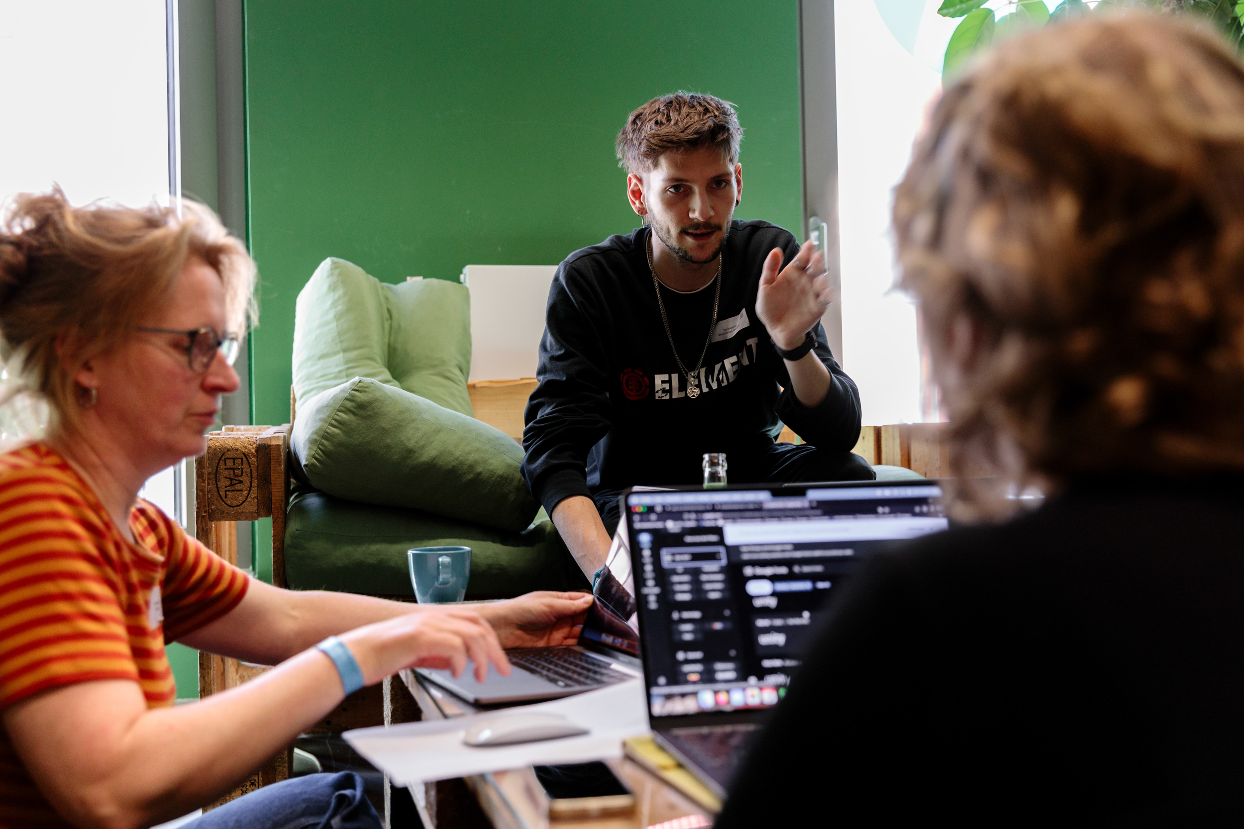 Drei Menschen sitzen um einen Tisch und besprechen etwas am Laptop.